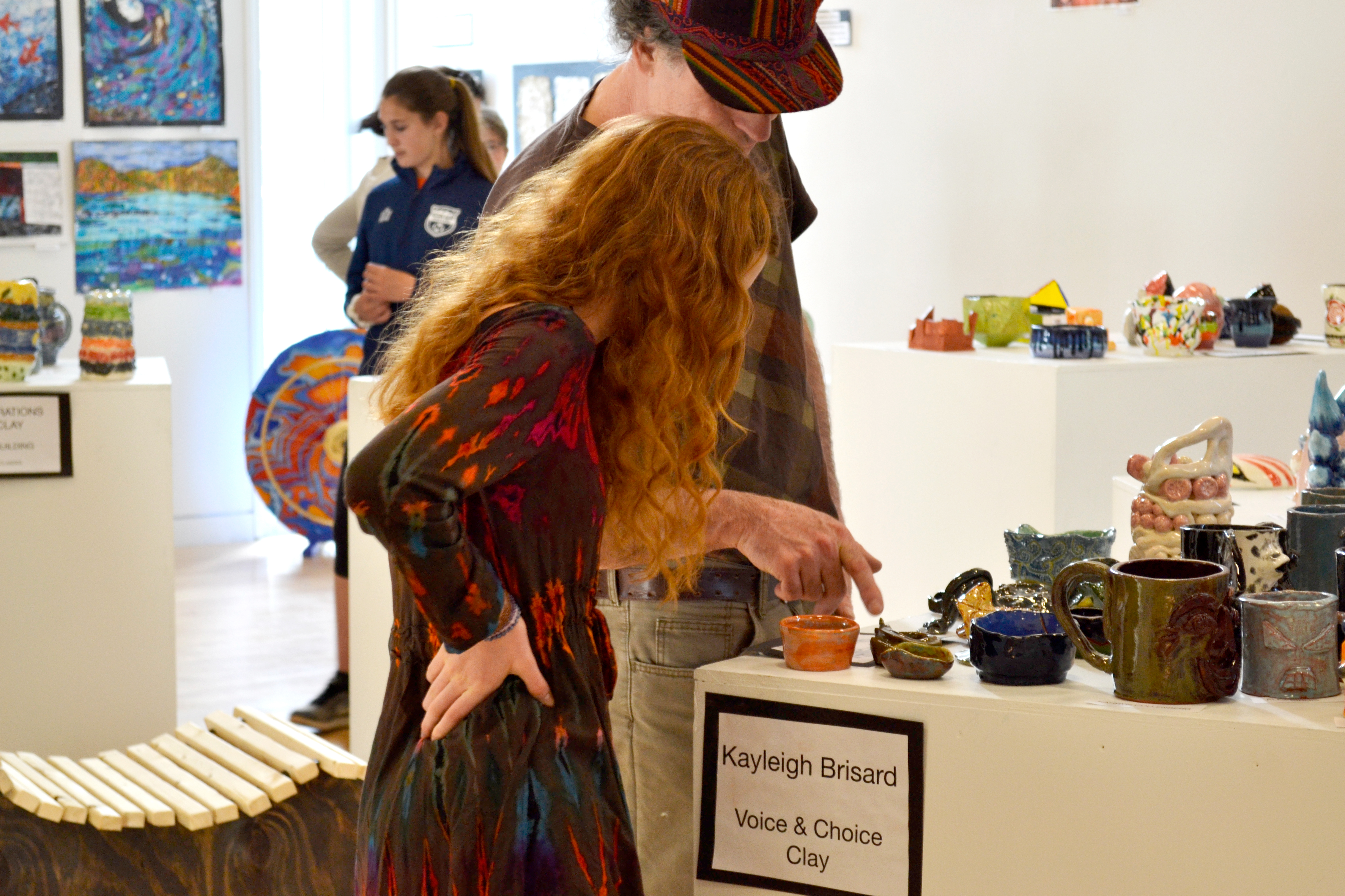 A girl watches as a man points at a sculpted piece.