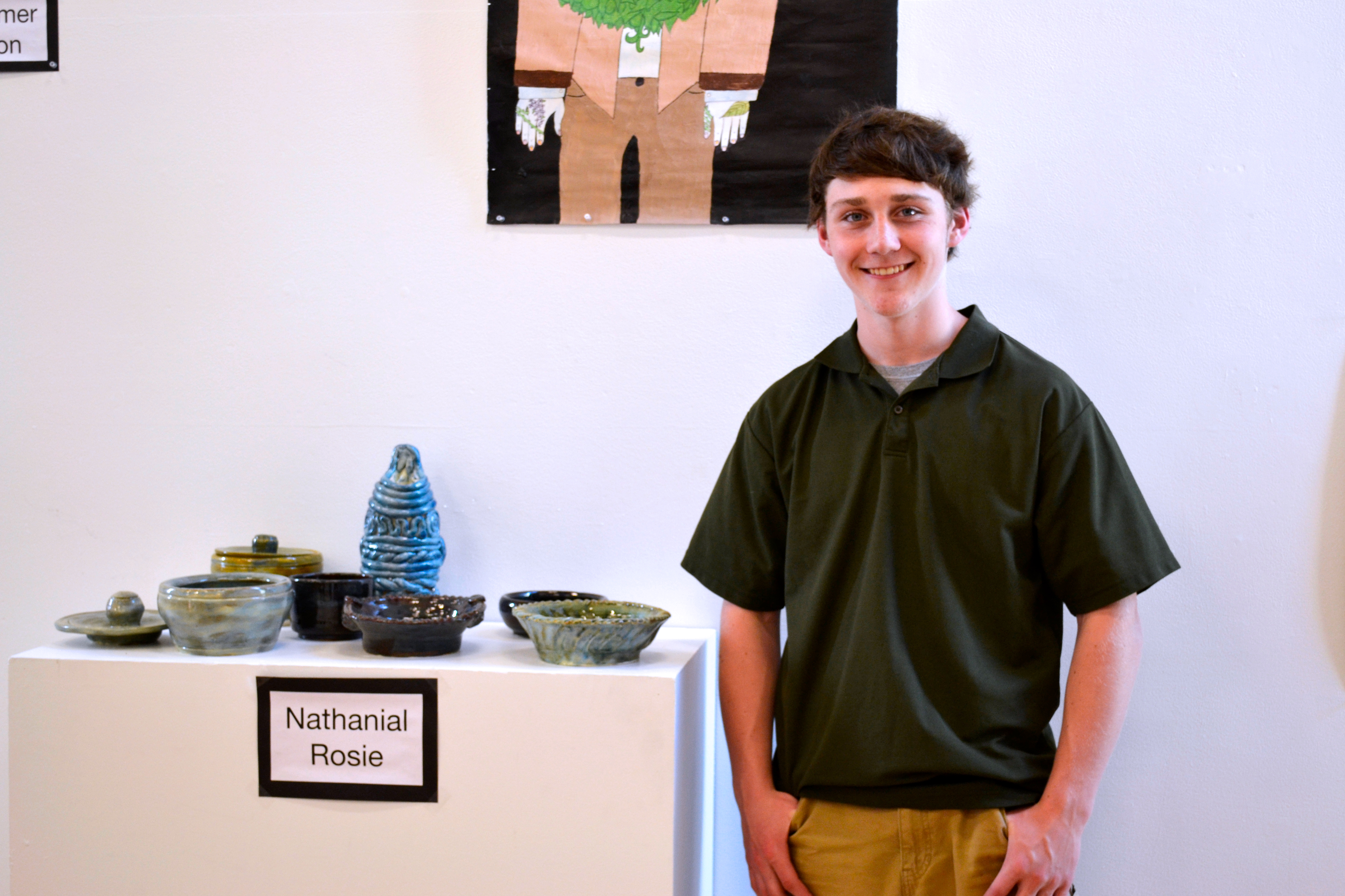 A student artist stands with his pottery work.