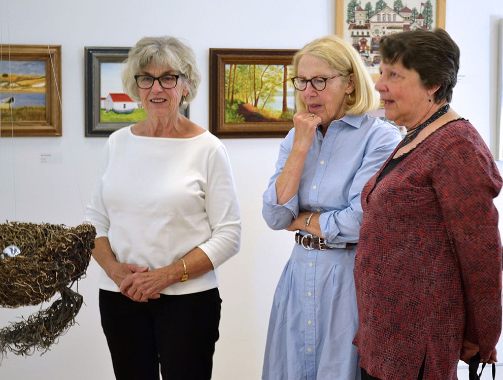 Three observers gather around an artwork.