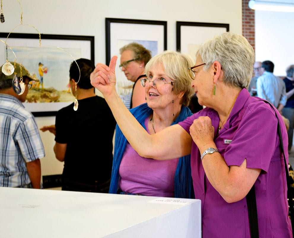 Two people discuss a piece of art and the GoldLEAF opening reception.