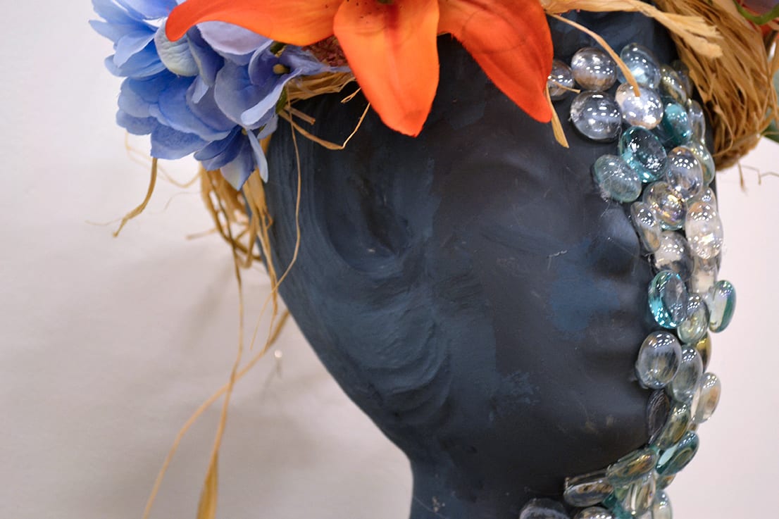 A female form is covered in flowers and stones.